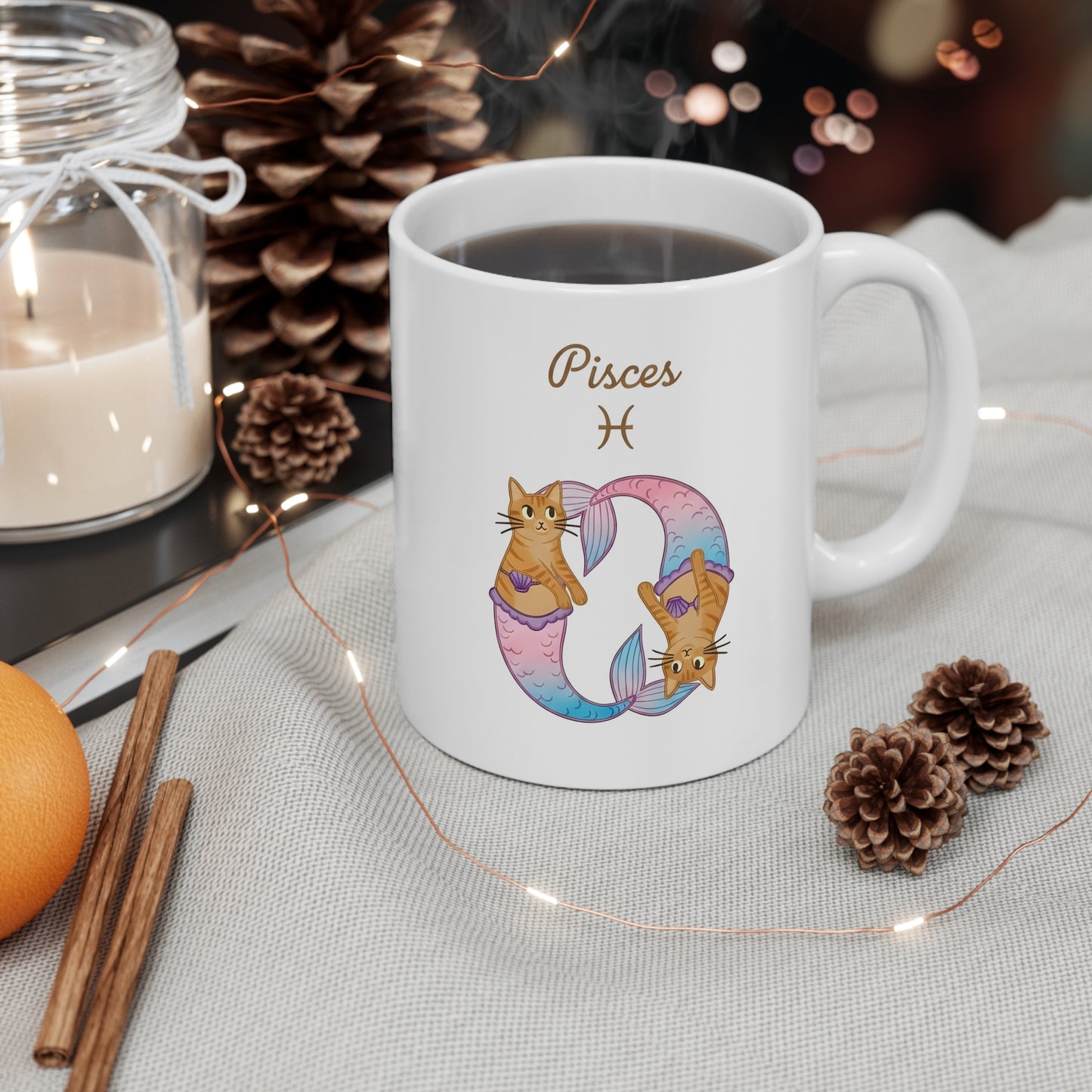 White mug with Pisces zodiac design featuring cats, surrounded by decorative items on a table.